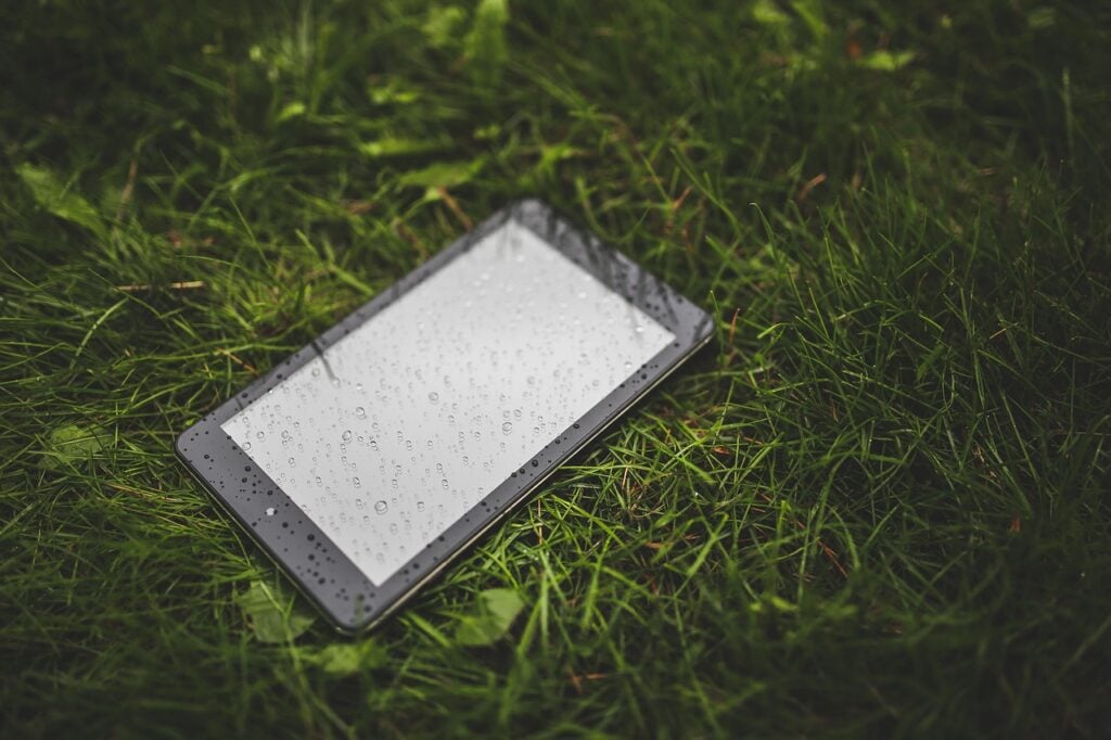 a tablet computer, face up on green grass, droplets of water on its surface