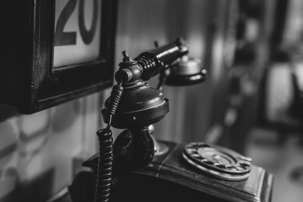 an old rotary telephone viewed from the side, with a frame with the number 20 in it on the wall behind it