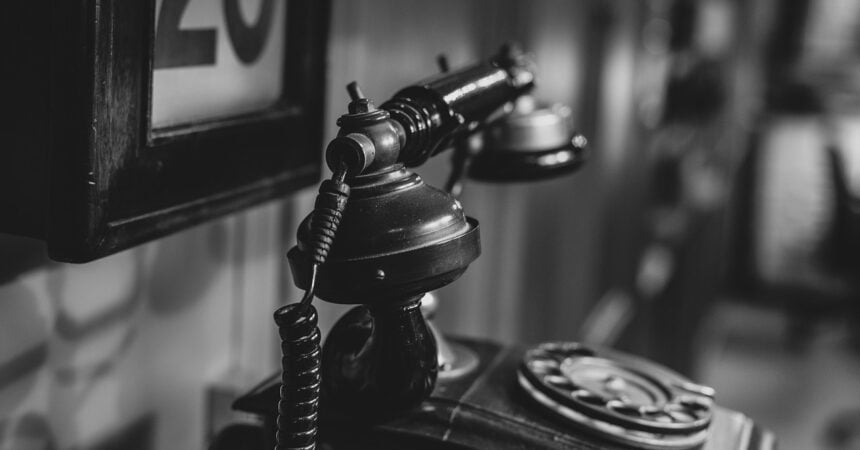 an old rotary telephone viewed from the side, with a frame with the number 20 in it on the wall behind it