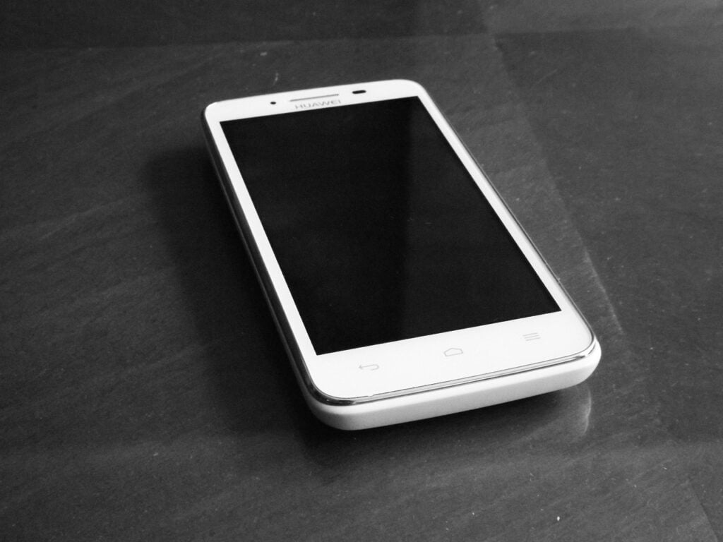 a white smartphone with a black screen sitting on a polished wood surface