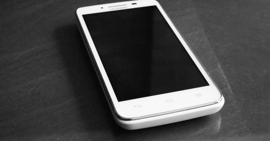 a white smartphone with a black screen sitting on a polished wood surface