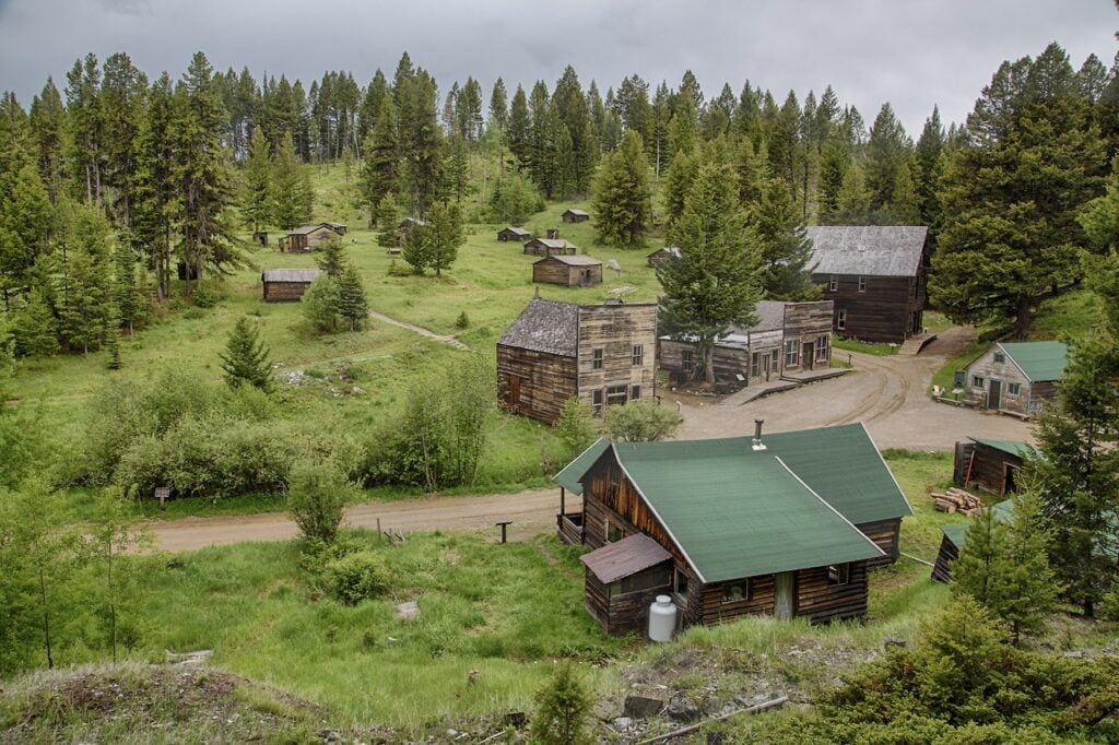 the preserved remains of the ghost town of Garnet, Montana, showing wooden buildings with green roofs amidst a green and verdant landscape