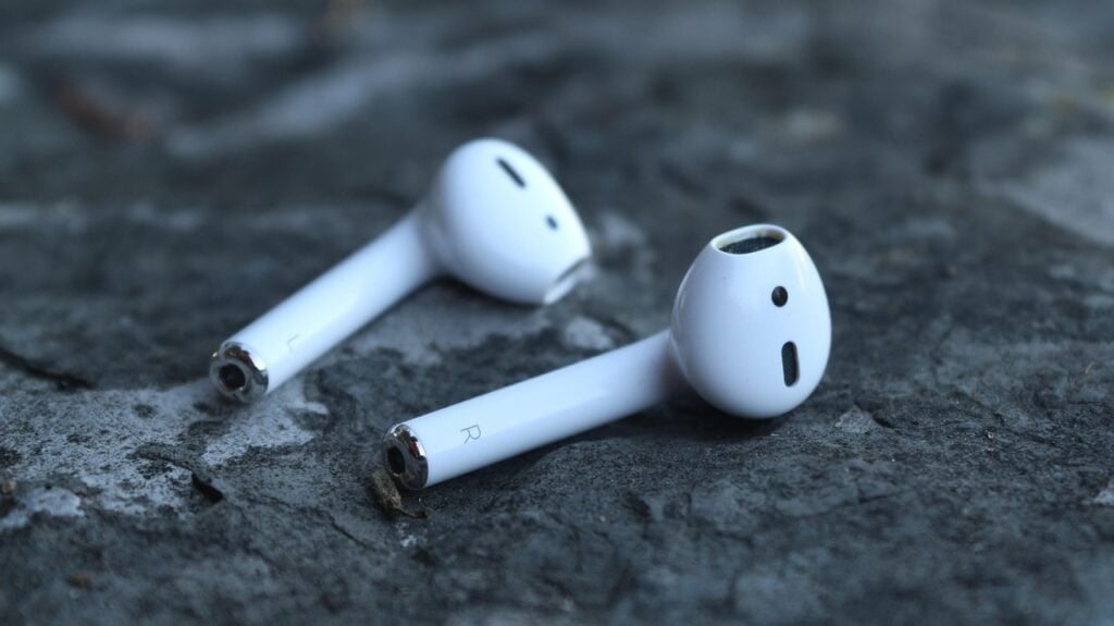 white wireless earbuds, slightly battered looking, lying on a rugged stone surface