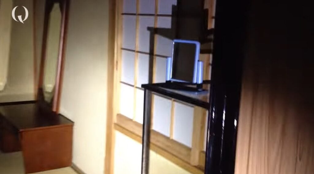 the interior of a modern japanese home, in ruins. there are shoji panels on the walls, a shelving unit, and a Japanese-style dressing table with a mirror present. it is very dark.