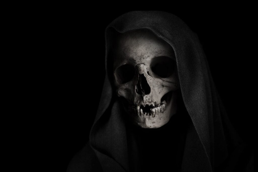 a human skull draped in a black hood against a black background