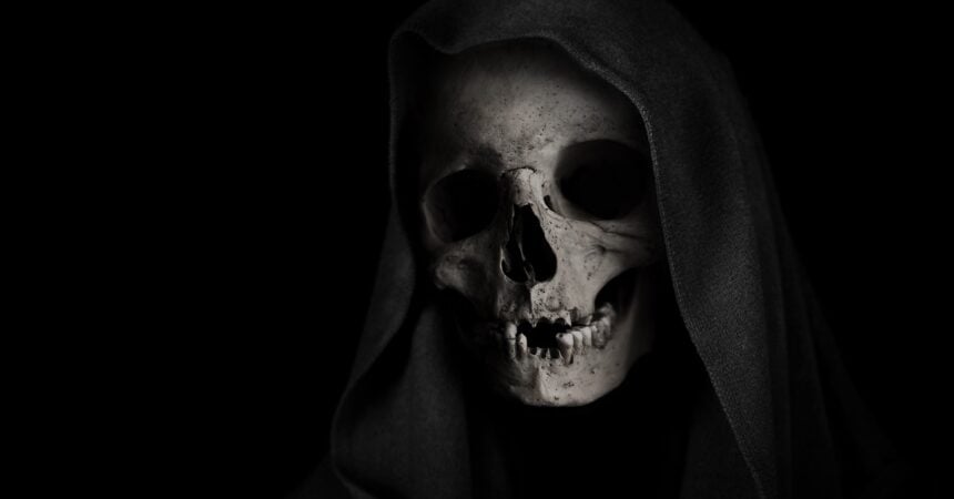 a human skull draped in a black hood against a black background