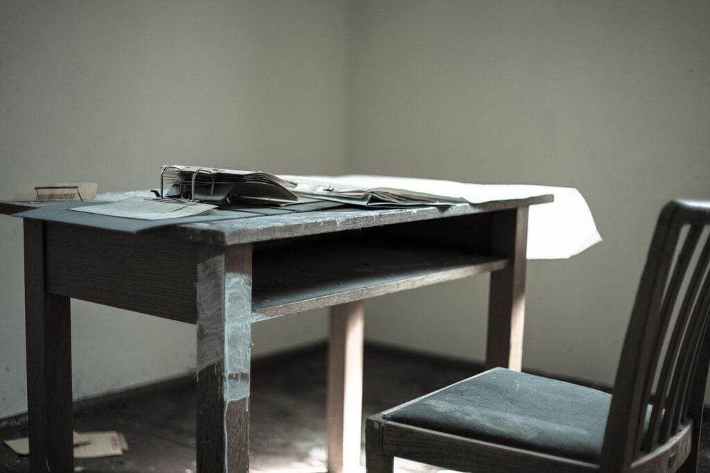 an old, dusty, wooden school desk and chair with papers on it in an abandoned school room