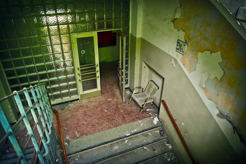 looking down stairs at an open glass door in an abandoned building