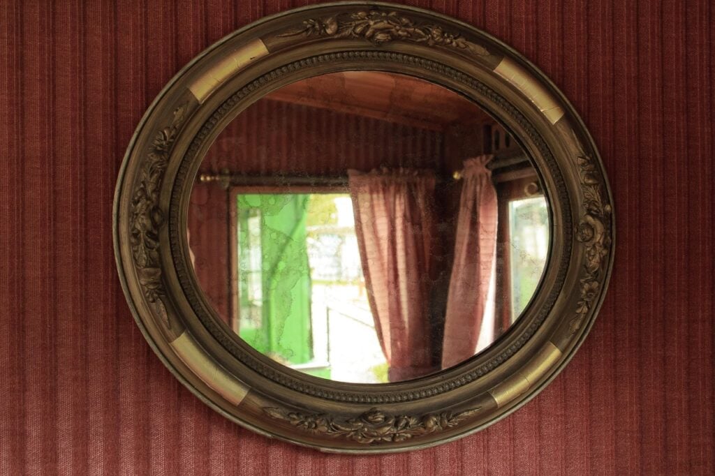 a round mirror with a gold frame hung on a wall with red striped wallpaper