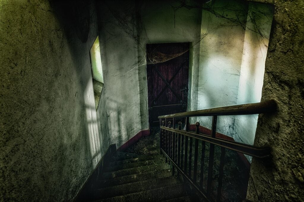 looking down a staircase in an abandoned building towards a landing with a closed wood door