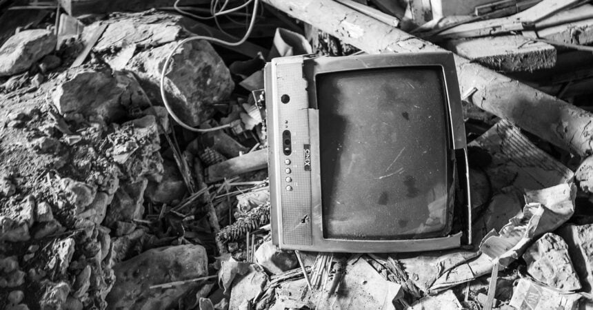 an old, broken, CRT television lying on its side amidst the ruins of a building